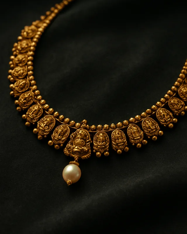 A 22 karat gold temple necklace with a pearl drop, on dark velvet